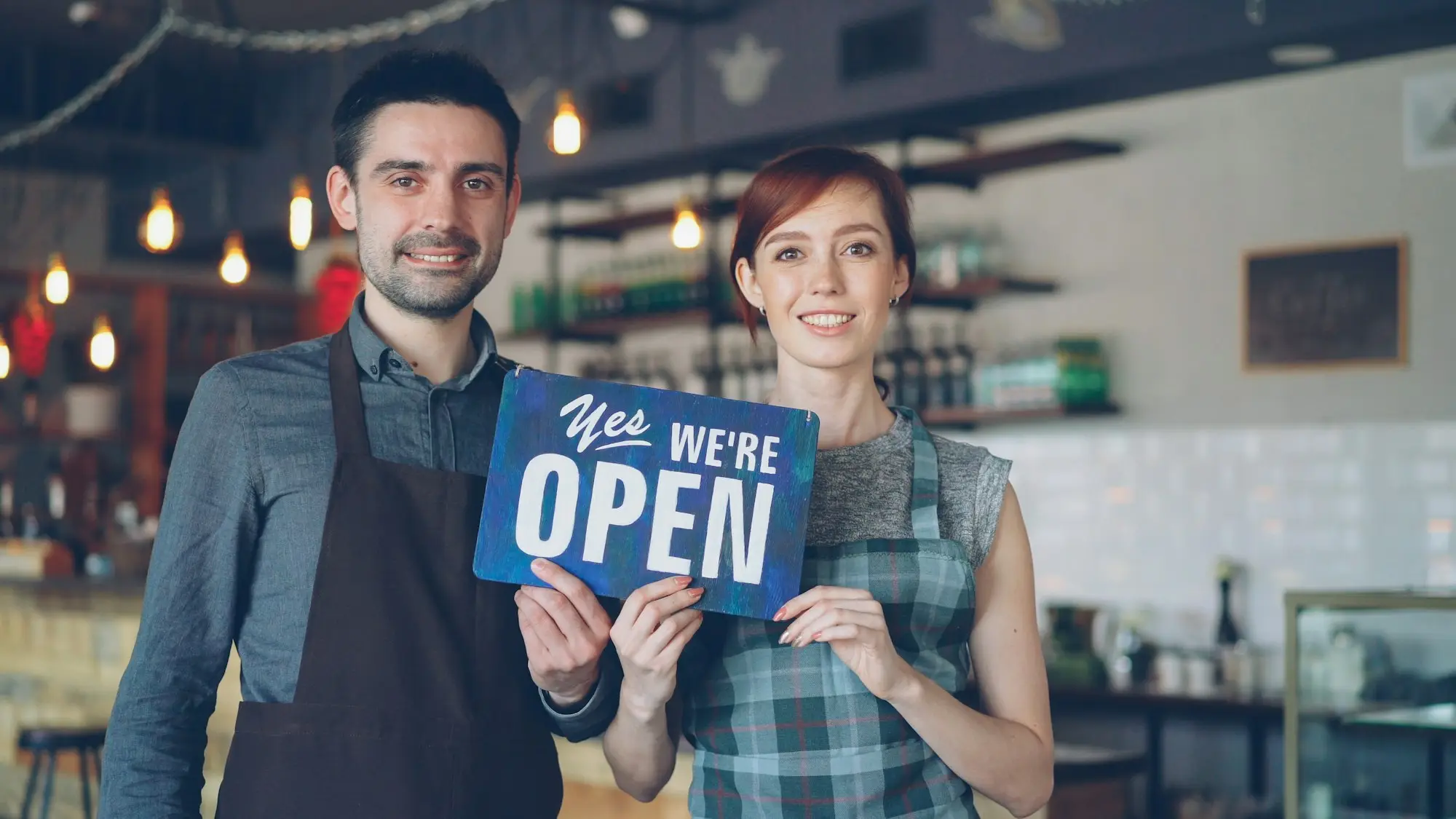 New owners holding an open sign in the shop they bought with a business acquisition loan