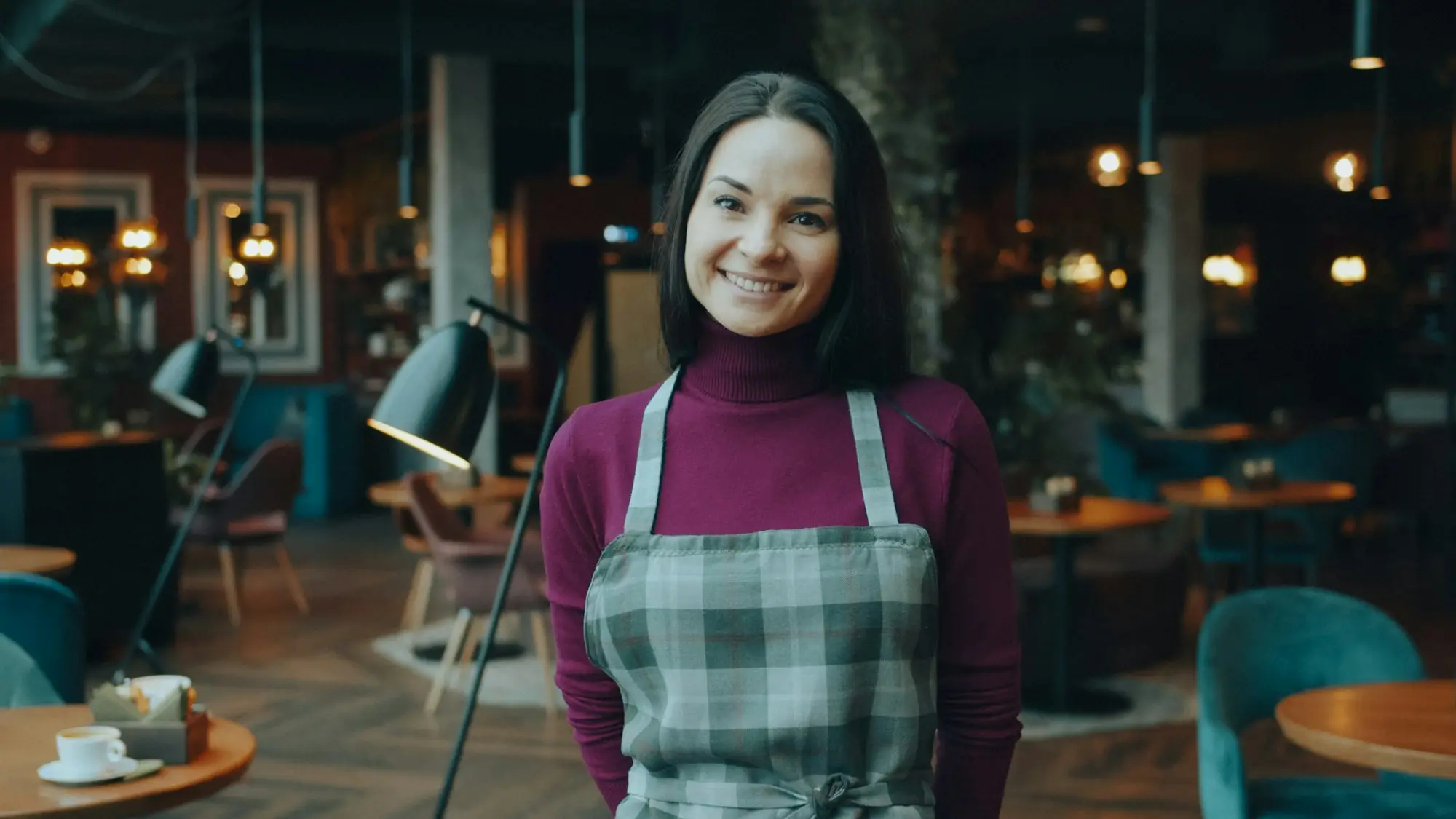 Smiling café owner in an apron standing in her restaurant, a business owner exploring business loans