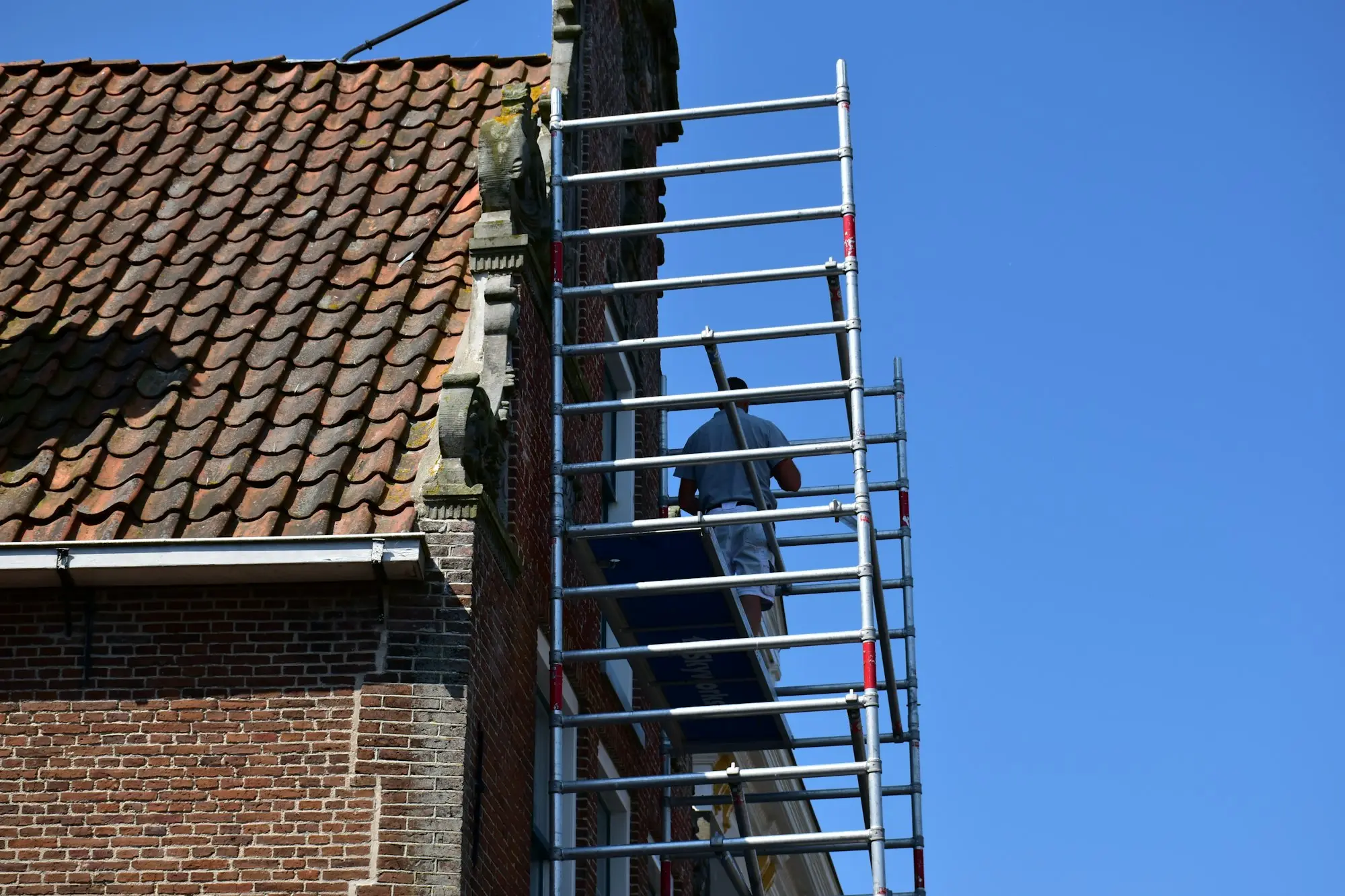Painter rolling fresh paint onto the exterior wall of a house during a residential repaint