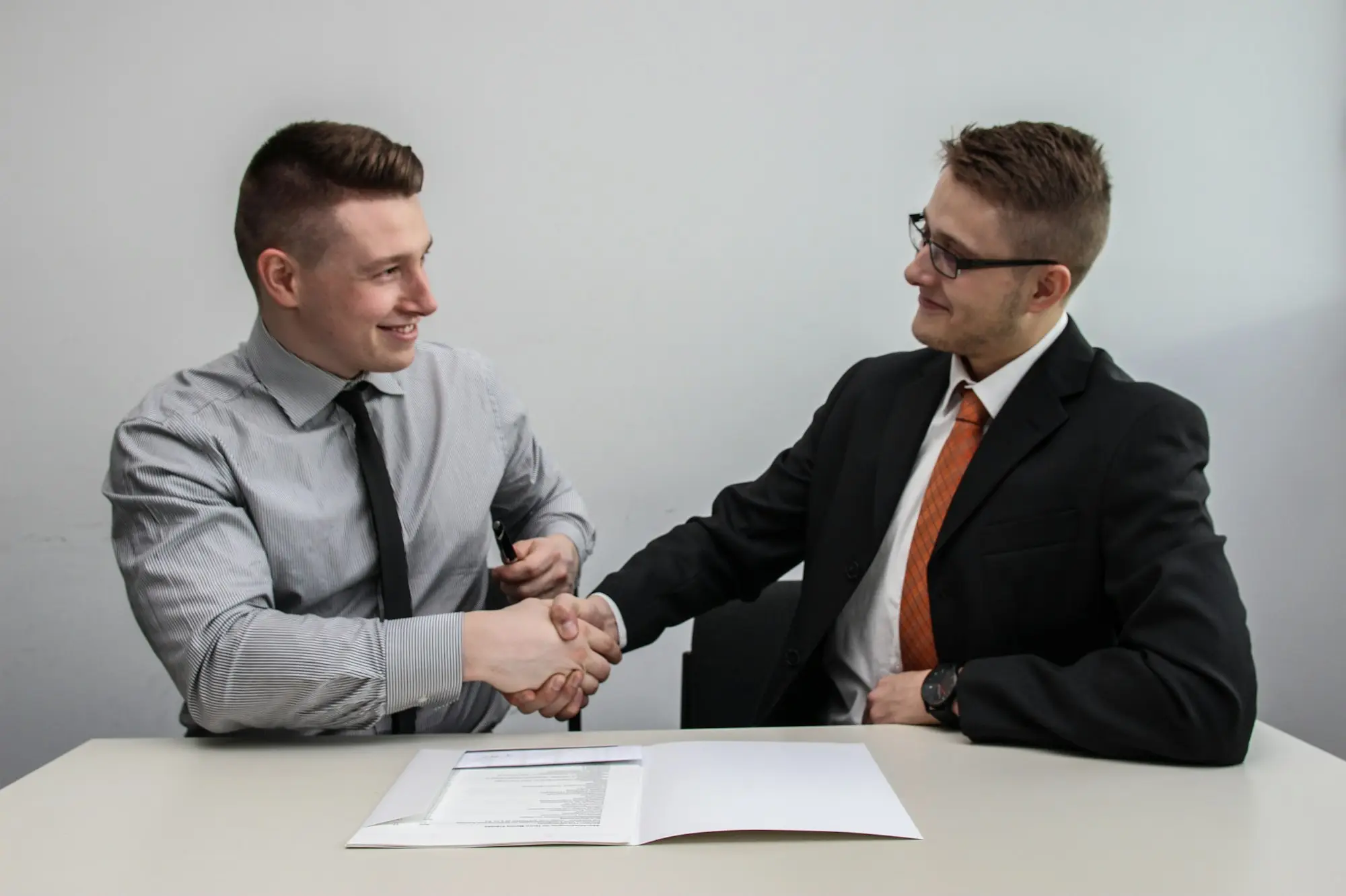 Two business partners shaking hands in a small office after a new director joins, ahead of an unsecured business loan